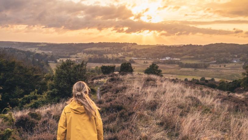 Jente i gul jakke vandrer langs en sti i solnedgang gjennom Rebild Bakken, Danmark